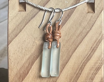 May include: A pair of earrings with clear glass rectangular pendants and brown leather cord accents.