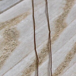 May include: A delicate necklace featuring a light pink teardrop-shaped pendant and clear, faceted beads. The necklace is strung on a thin, brown cord and has a silver clasp.