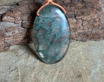May include: A green and brown agate pendant on a brown leather cord. The pendant is oval shaped and has a natural, organic look.