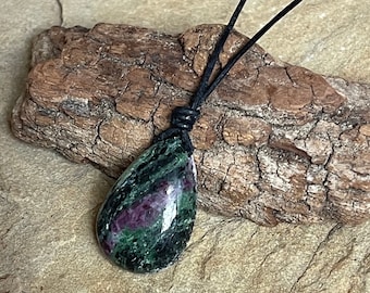 May include: A teardrop-shaped green and pink gemstone pendant on a black leather cord necklace.