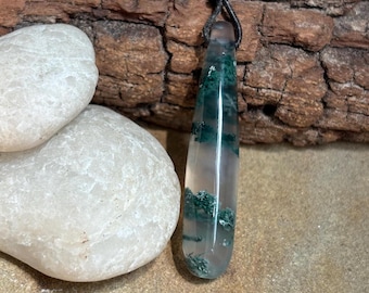 May include: A green moss agate pendant on a brown leather cord. The pendant is a teardrop shape and has a clear, translucent appearance with green moss inclusions.