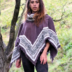 Peut inclure: Un poncho violet foncé doté d'un col montant et d'une bordure blanche avec un motif géométrique noir. Le vêtement présente un ourlet en forme de V fini avec des détails à franges le long des bords, donnant un aspect texturé au tissu.