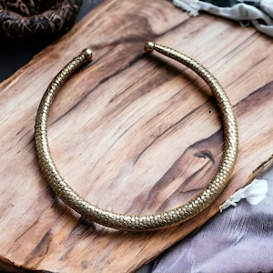 May include: A gold-toned choker necklace with a textured, snake-like design. The necklace is displayed on a wooden surface.