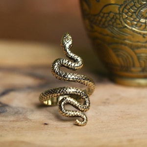 May include: A gold-toned snake ring with a coiled design. The ring is made of metal and has a textured surface.