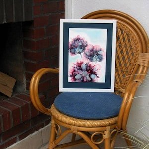Può includere: Dipinto ad acquerello incorniciato di tre fiori rosa e blu su sfondo bianco. Il dipinto è in una cornice bianca con un passepartout blu scuro.