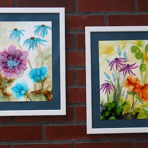 Può includere: Due dipinti incorniciati di composizioni floreali. Il dipinto a sinistra presenta un fiore rosa con fiori blu e foglie. Il dipinto a destra presenta un fiore arancione brillante con fiori viola e foglie verdi.