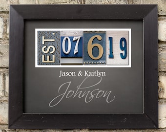 May include: Framed artwork with a black border, featuring the text "EST. 07 6 19" in decorative letters. Below, the names "Jason & Kaitlyn" and "Johnson" are displayed in elegant script. The artwork is set against a gray background.