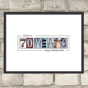 May include: Framed print with the words "Cheers to... 70 YEARS Happy Birthday Bob!" The numbers and letters are composed of various images, including a traffic light, tools, and a climbing carabiner. The frame is black.