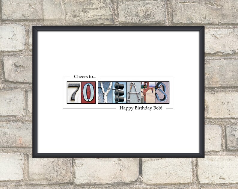 May include: Framed print with the words "Cheers to... 70 YEARS Happy Birthday Bob!" The numbers and letters are composed of various images, including a traffic light, tools, and a climbing carabiner. The frame is black.