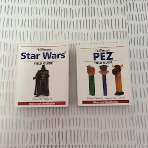 May include: Two small, white, paperback books with colorful covers. The book on the left is a Star Wars field guide with a picture of Darth Vader. The book on the right is a PEZ field guide with a picture of three PEZ dispensers.