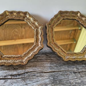 May include: Two octagonal mirrors featuring ornate, textured gold-toned frames with scalloped edges. The reflective glass surfaces are clear, and the frames exhibit a detailed, embossed pattern throughout their entire perimeter and border.