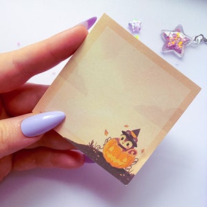 May include: A beige sticky note with a cartoon illustration of an owl wearing a witch hat and sitting in a pumpkin. The illustration is in the bottom right corner of the note.