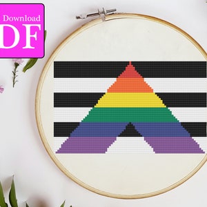 Puede incluir: Un patrón de punto de cruz con un fondo a rayas blanco y negro y un triángulo arcoíris en el centro. El patrón está en un aro de bordado de madera.