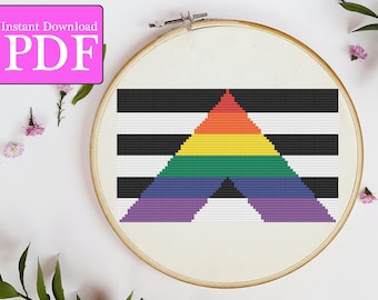 May include: A cross-stitch pattern featuring a black and white striped background with a rainbow triangle in the center. The pattern is in a wooden embroidery hoop.