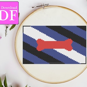 Könnte beinhalten: Ein Kreuzstichmuster einer blauen, schwarzen und weißen Flagge mit einem roten Knochen in der Mitte. Die Flagge befindet sich in einem hölzernen Stickrahmen.