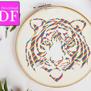May include: A rainbow colored tiger head cross stitch pattern. The tiger's stripes are made up of different colors of the rainbow. The pattern is in a white embroidery hoop.