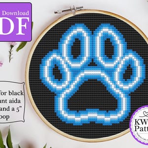 Op de afbeelding: Een kruissteekpatroon van een blauw en witte pootafdruk op zwarte stof, omlijst in een houten hoepel. De afbeelding bevat tekst die zegt "Instant Download PDF" en "KW Patterns". Het patroon is ontworpen voor een hoepel van 12.7 cm.
