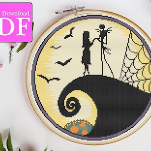 以下が含まれることがあります： ナイトメア・ビフォア・クリスマスのジャック・スケリントンとサリーをフィーチャーしたクロスステッチパターン。パターンは、満月を背に丘の上に立っている様子を描いています。月は黄色で、黒い三日月形と紫色の輪郭があります。丘は黒で、黄色の渦巻き模様があります。パターンは木製の刺繍枠に入っています。