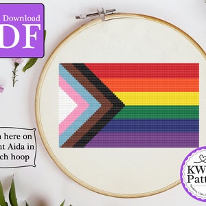 May include: A cross-stitch pattern of the Progress Pride flag, a variation of the rainbow pride flag with black and brown stripes to represent people of color and a light blue, pink, and white arrow to represent transgender people. The pattern is shown on 18 count Aida fabric in a 6-inch hoop.