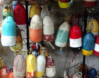 Pode incluir: Uma coleção de boias redondas e cilíndricas coloridas com vários padrões e designs. As boias são feitas de madeira e pintadas de vermelho, azul, amarelo, verde, branco e preto. Algumas das boias têm números e letras pintadas nelas.