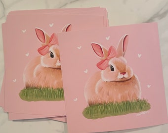 May include: Two pink cards with a pink bunny rabbit wearing a pink bow on each card. The background is pink with white hearts.