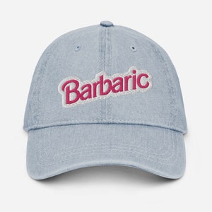 May include: A light blue denim baseball cap with the word "Barbaric" embroidered in pink and white letters.