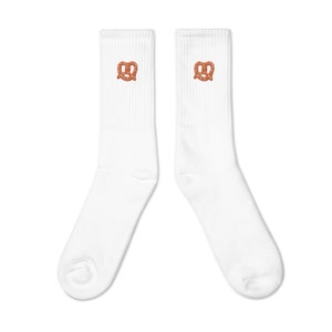 May include: Pair of white crew socks with a small, orange pretzel image embroidered on each sock. The socks are made of a soft, comfortable material and are perfect for everyday wear.  These casual socks feature a simple, minimalist design that is both stylish and versatile. The pretzel graphic adds a touch of fun and whimsy to the classic sock design.