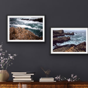 May include: Two framed photographs of ocean waves crashing against rocky shorelines. The top photo shows a close-up of the rocks and waves, while the bottom photo shows a wider view of the coastline.