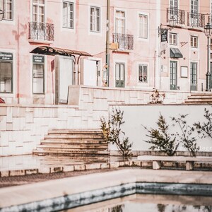 Puede incluir: Un reflejo de un edificio rosa con ventanas y balcones en una peque&ntilde;a piscina de agua. El edificio se encuentra en un entorno urbano con una pared de ladrillo blanco y escalones en primer plano.