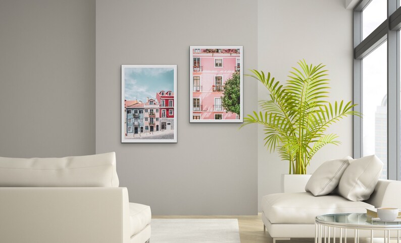 Op de afbeelding: Twee ingelijste foto's van kleurrijke gebouwen in een stad. De foto links toont een rij gebouwen met blauwe, groene en rode gevels. De foto rechts toont een roze gebouw met witte versieringen en een boom ervoor.