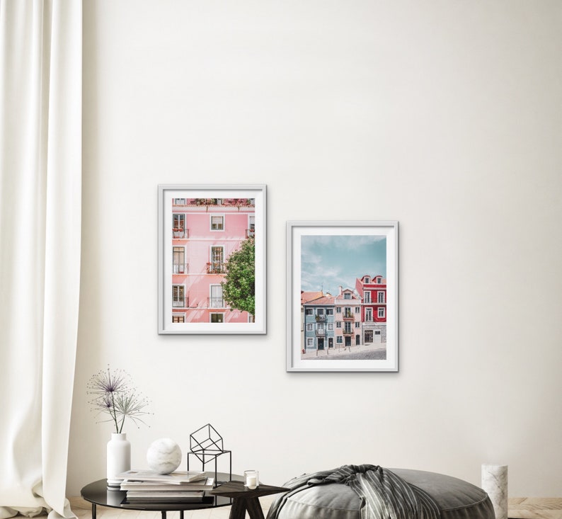 Op de afbeelding: Twee ingelijste foto's van kleurrijke gebouwen in een stad. De eerste foto toont een roze gebouw met witte versieringen en een groene boom ervoor. De tweede foto toont een rij kleurrijke gebouwen met blauwe, roze en rode gevels.