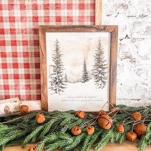 May include: A framed print with a wintery forest scene and the text "Glory to God in the highest, and on earth peace, goodwill toward men." The print is surrounded by a garland of evergreen branches with brown jingle bells.