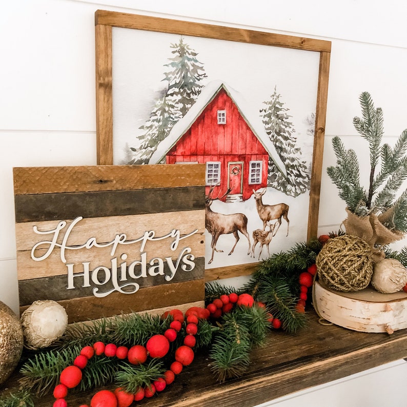 May include: A wooden sign with the text "Happy Holidays" in white lettering, a red cabin with snow on the roof, and a Christmas tree with red berries and a gold ornament.