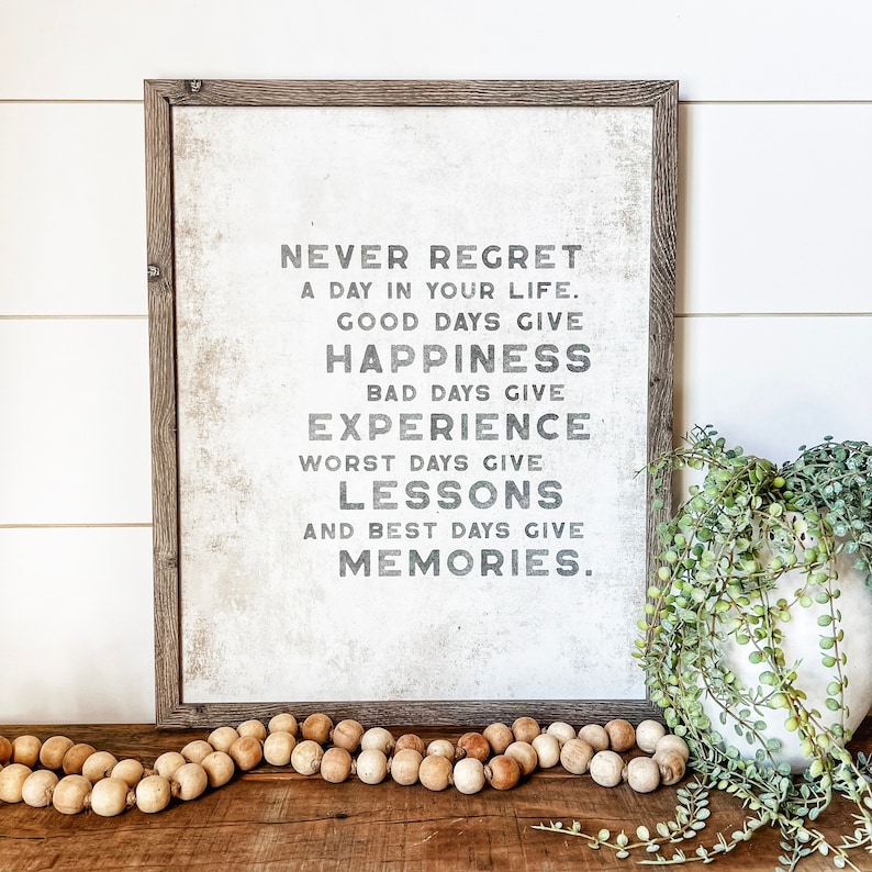 May include: A framed print with a white background and black text that reads "Never regret a day in your life. Good days give happiness. Bad days give experience. Worst days give lessons. And best days give memories."