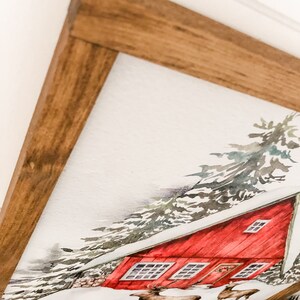 May include: A watercolor painting of a red cabin in a snowy forest. The cabin has a white roof and a brown door. There are two deer in the foreground.