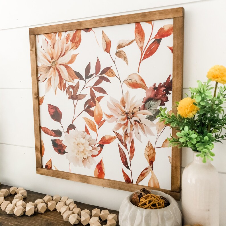 May include: A framed watercolor print with a floral design featuring brown, orange, and white flowers on a white background. The frame is made of wood and has a brown stain.