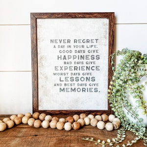 May include: A framed print with a white background and black text that reads "Never regret a day in your life. Good days give happiness. Bad days give experience. Worst days give lessons. And best days give memories."