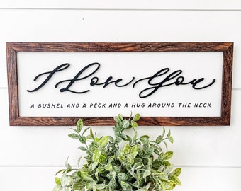 May include: A framed wooden sign with the words "I Love You" in a cursive font. Below the text is the phrase "A bushel and a peck and a hug around the neck." The sign has a white background and a dark brown frame.