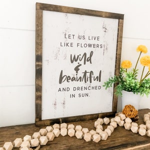 Pu&ograve; includere: Un cartello di legno con sfondo bianco e testo marrone che recita "Let us live like flowers wild & beautiful and drenched in sun."