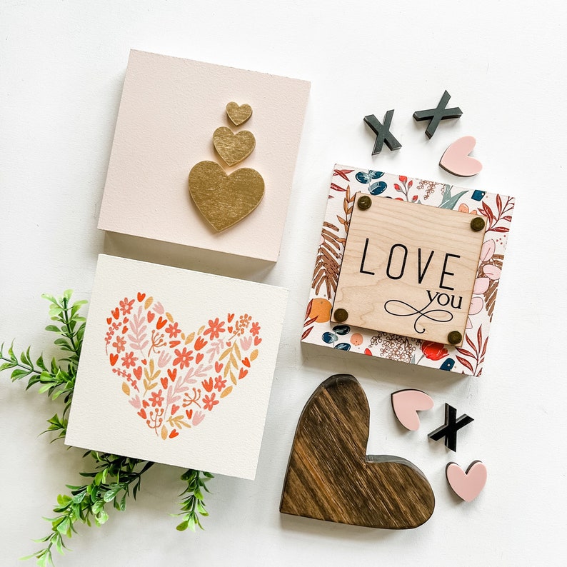 May include: A set of four wooden signs with a Valentine's Day theme. The signs feature hearts, floral patterns, and the text "Love You".