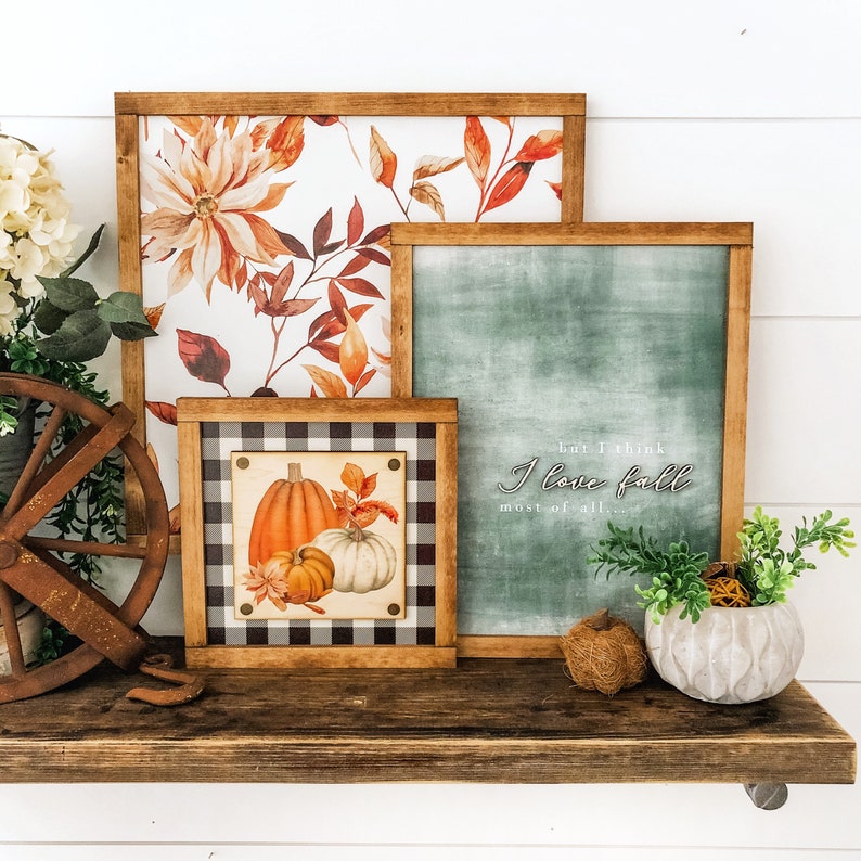 Peut inclure: Plusieurs tableaux encadr&eacute;s sur le th&egrave;me de l'automne. L'un pr&eacute;sente un motif floral avec des feuilles orange et marron, un autre a un fond vert avec le texte "but I think I love fall most of all...". Un troisi&egrave;me cadre affiche des citrouilles.