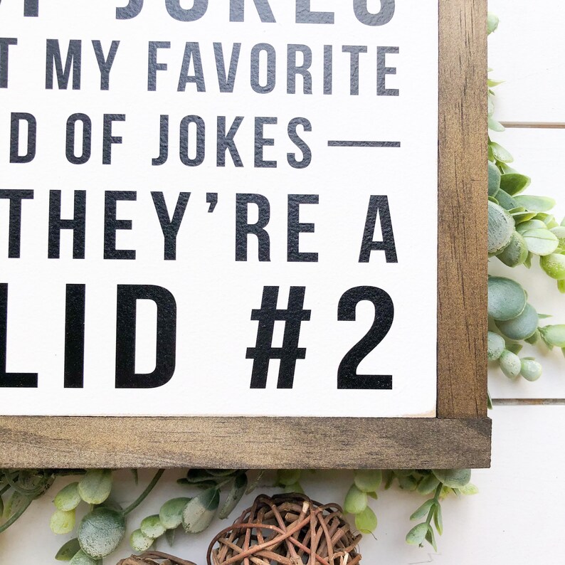 Puede incluir: Un letrero de madera blanco con texto negro que dice "Dad Jokes - They're a  #2  -  Not My Favorite Kind Of Jokes". El letrero est&aacute; enmarcado en un marco de madera marr&oacute;n oscuro.