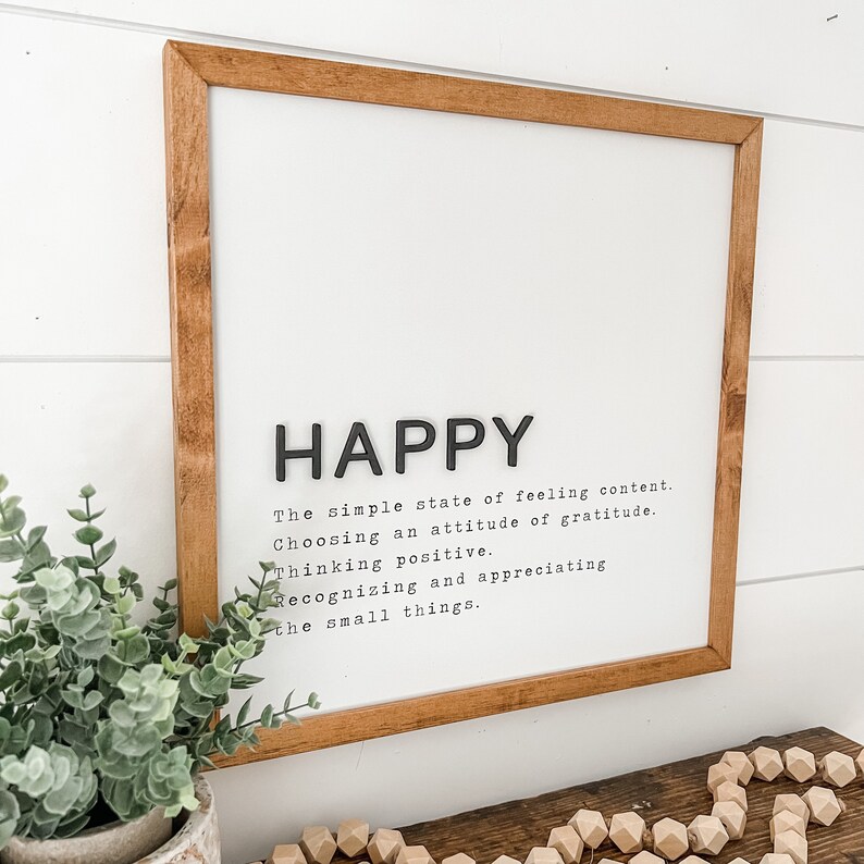 May include: A framed print with the word "HAPPY" in large black letters. The print defines happiness as "The simple state of feeling content. Choosing an attitude of gratitude. Thinking positive. Recognizing and appreciating the small things."