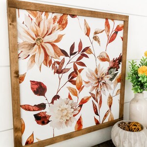 May include: A framed print with a watercolor design of fall leaves and flowers in shades of orange, brown, and white on a white background.