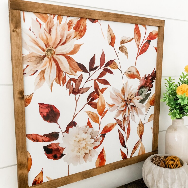 May include: A framed print with a watercolor design of fall leaves and flowers in shades of orange, brown, and white on a white background.