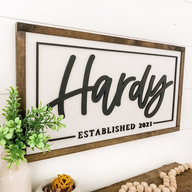 May include: A wooden sign with a white background and black lettering. The sign says "Hardy Established 2021".