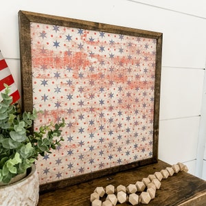 May include: A framed wood sign with a distressed American flag design featuring red, white, and blue stars and dots. The sign is perfect for patriotic decor.