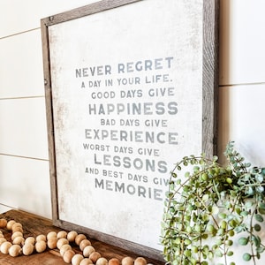 May include: A framed sign with a white background and gray text that reads "Never regret a day in your life. Good days give happiness. Bad days give experience. Worst days give lessons. And best days give memories."
