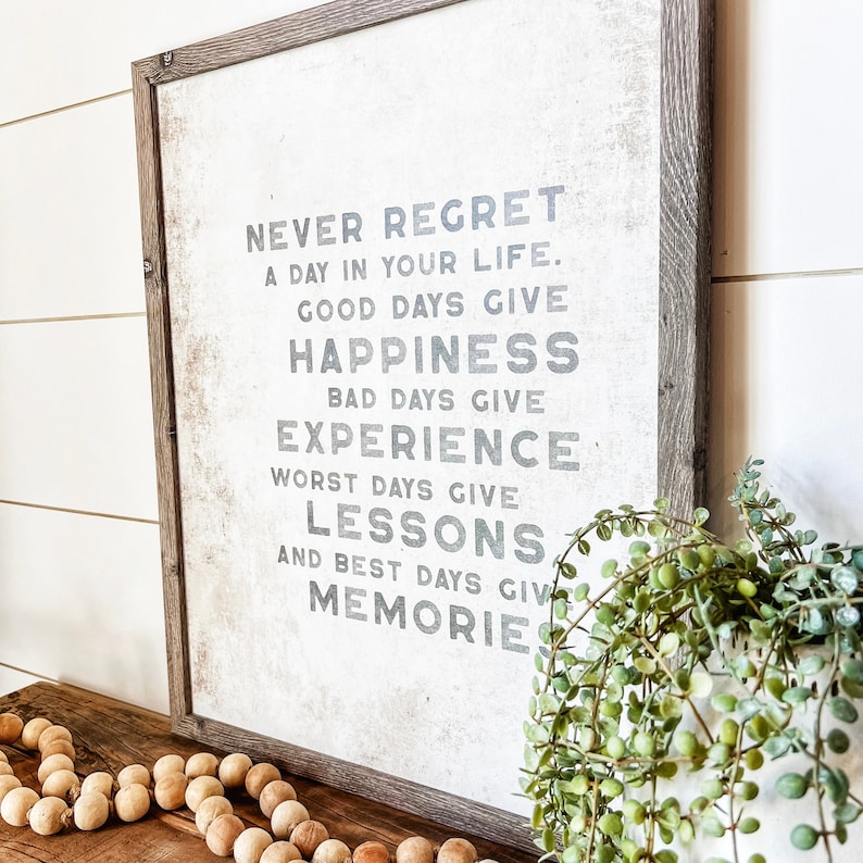 May include: A framed sign with a white background and gray text that reads "Never regret a day in your life. Good days give happiness. Bad days give experience. Worst days give lessons. And best days give memories."