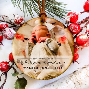 May include: A round wooden ornament with a photo of a baby sleeping. The ornament has the text "my very first Christmas" and "WALKER JUNE | 2021" printed on it.